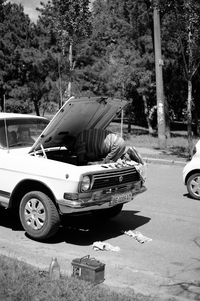 A man repairing a vintage car on a street in a monochrome scheme.